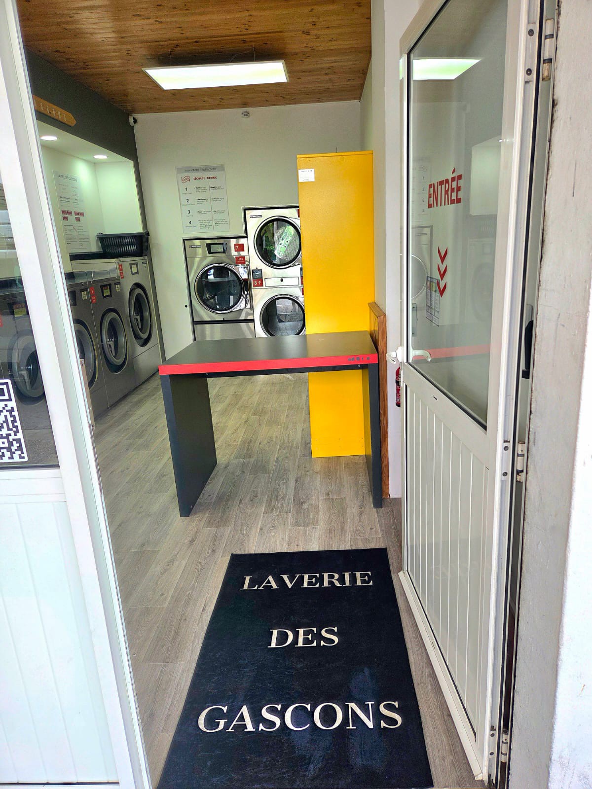 Entrée côté sèche-linge — vue sur les machines et la table de pliage